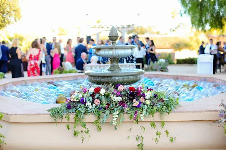 Flower-adorned fountain at an outdoor event with guests in the background