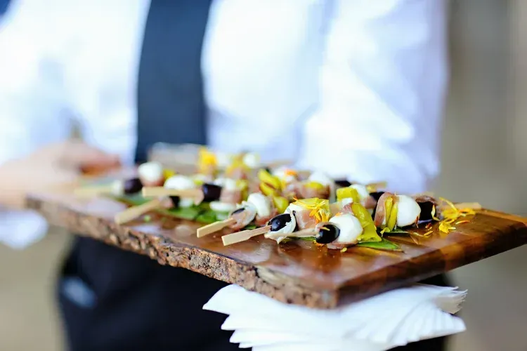 Waiter carrying a wooden tray of garnished appetizers on white napkins