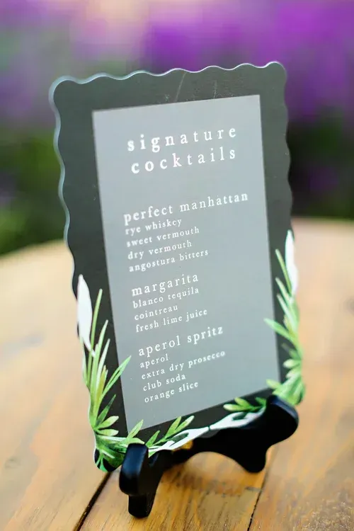 Black cocktail sign on a wooden table with white text and green leaf decorations