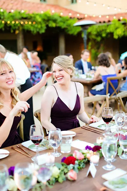 Guests socializing at a decorated outdoor banquet table with wine glasses and flowers