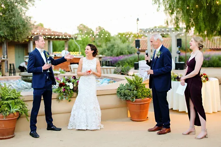 Outdoor wedding ceremony with bride and groom exchanging vows beside two attendants in formal attire.