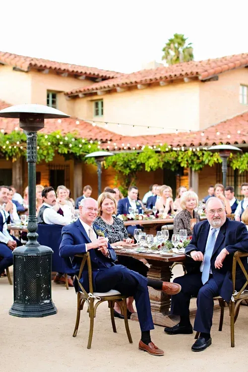 Guests seated at outdoor tables in a courtyard restaurant under a tiled roof, with drinks and a patio heater.