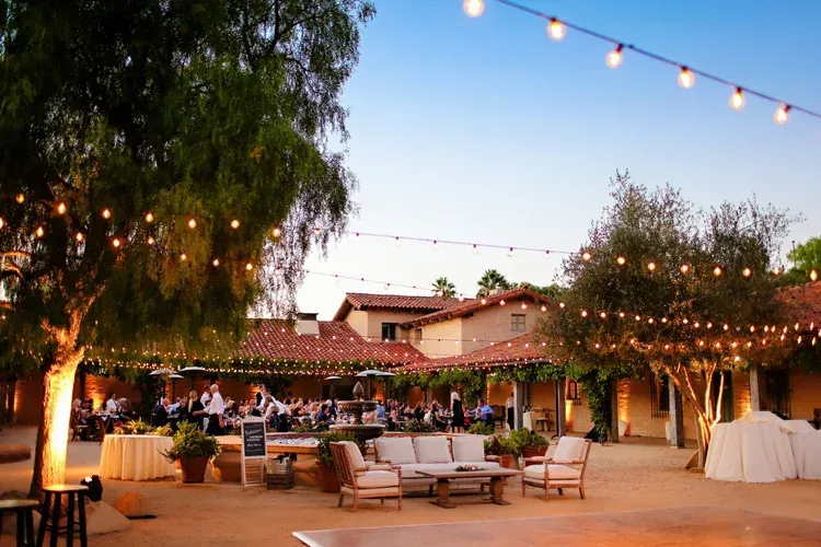 Festive outdoor patio at dusk with string lights, tables, and lounge seating beside a house