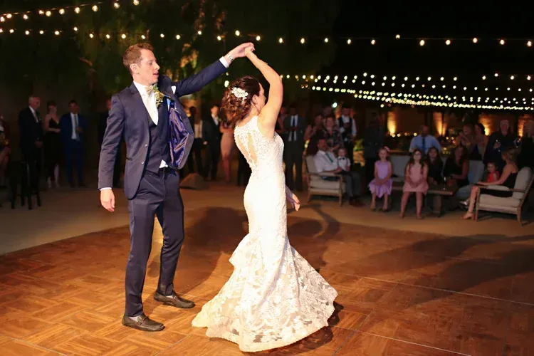 Bride twirls with groom on a dance floor at an outdoor evening wedding under string lights