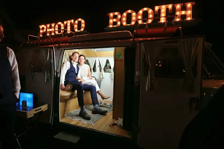 Neon-lit photo booth with two people seated inside, smiling for a picture.
