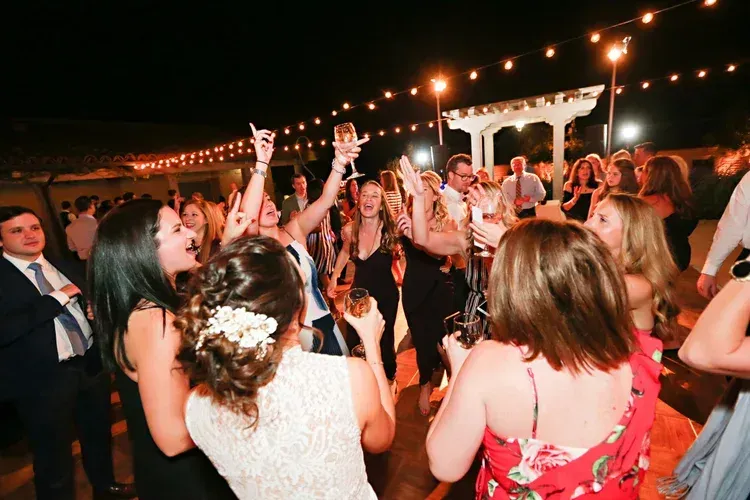 Guests dancing and raising glasses at an outdoor evening party under string lights