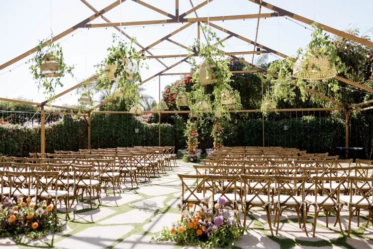 Outdoor wedding ceremony setup under a white canopy with rows of chairs and hanging greenery