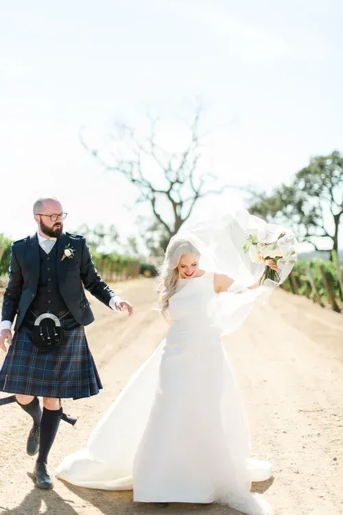 Bride and groom walking on a sandy road, the bride twirling her dress in a bright outdoor setting