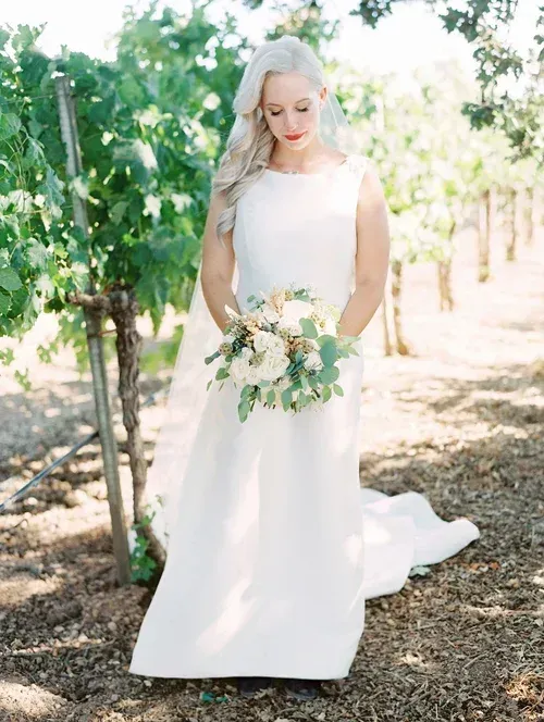 Bride in a white dress holding a bouquet in a sunlit vineyard