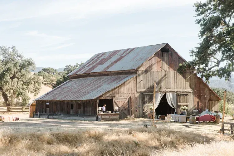 Rustic barn with weathered metal roof in a dry, rural field under a clear sky