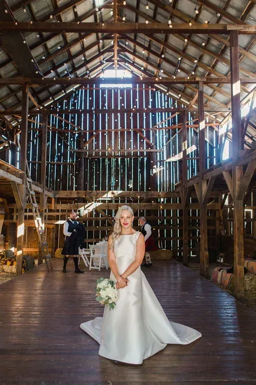 Bride in a white gown standing in a rustic barn wedding venue