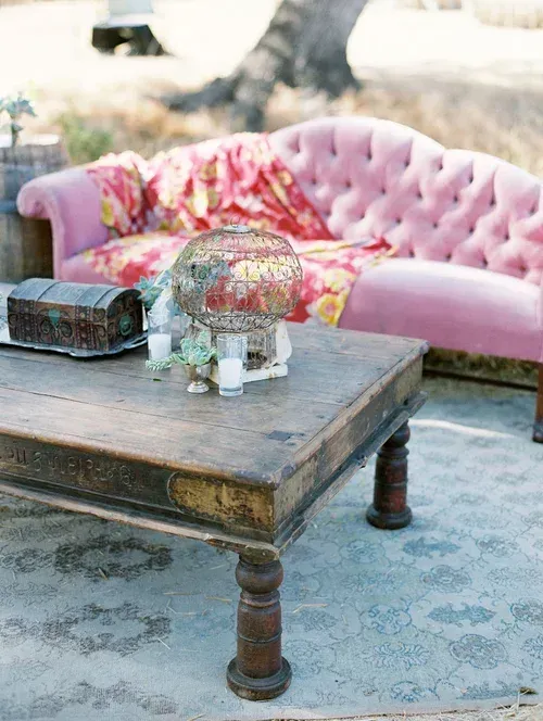 Vintage wooden coffee table with flowers in a glass dome, beside a pink tufted sofa outdoors