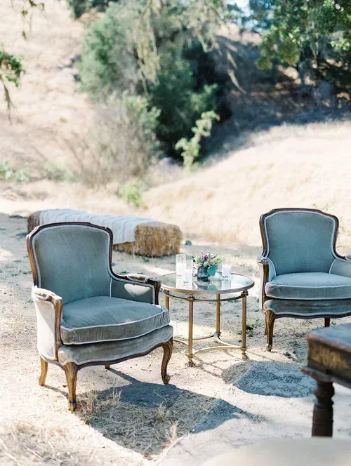 Two blue chairs and a glass table on a sunny outdoor patio with hills in the background