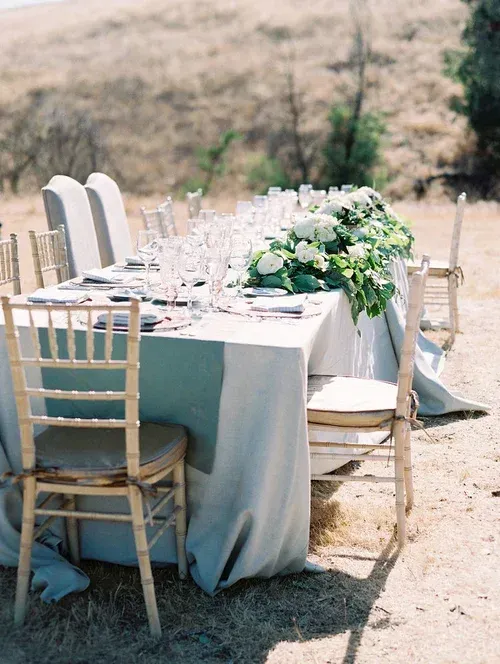 Outdoor banquet table with white chairs and floral centerpiece set in a dry field