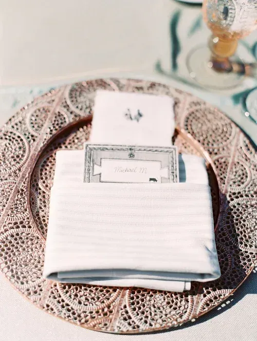 Folded white napkins with a place card on a lace charger at a set table
