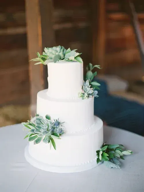 Three-tier white wedding cake with greenery on a table
