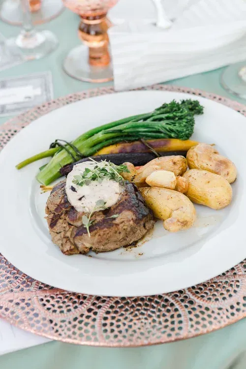Plated steak with potatoes and broccolini on a white table setting