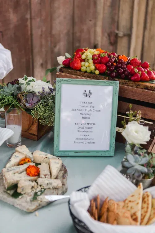 Buffet table with fruit platter, appetizers, and a framed menu card at a rustic event setup