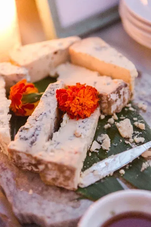 Cheese platter with marigold garnish on banana leaf, with plates and cups in the background