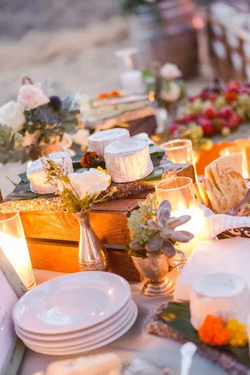 Outdoor table with candles, cakes, white plates, and floral decor at a warm-lit celebration