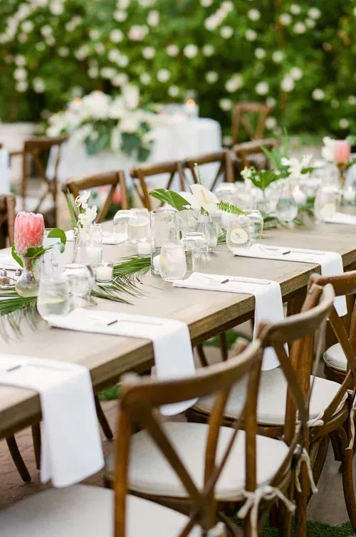 Elegant outdoor dining table with white linens, glassware, flowers, and wooden chairs