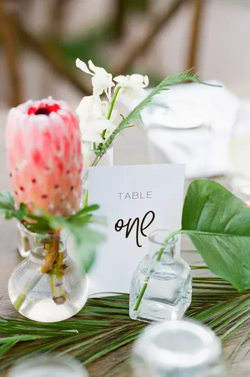 Table one card with pink flower, white blooms, greenery, and glass decor on a white table setting
