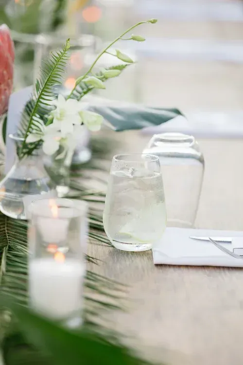 A candlelit table with glasses, greenery, and white napkins in a soft, elegant setting