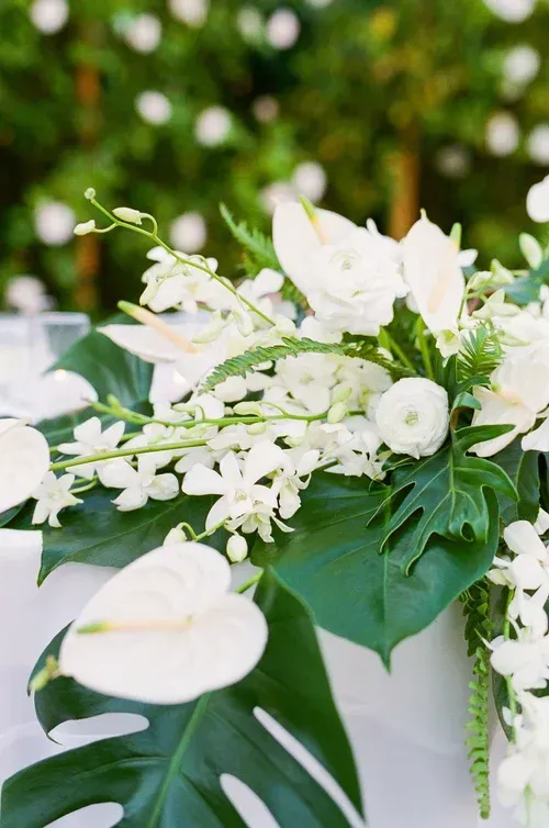 White flowers and green tropical leaves arranged in a bouquet against a soft blurred background