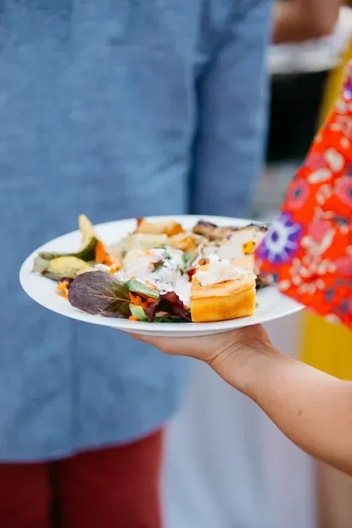Hand holding a white plate with assorted food at a festive gathering