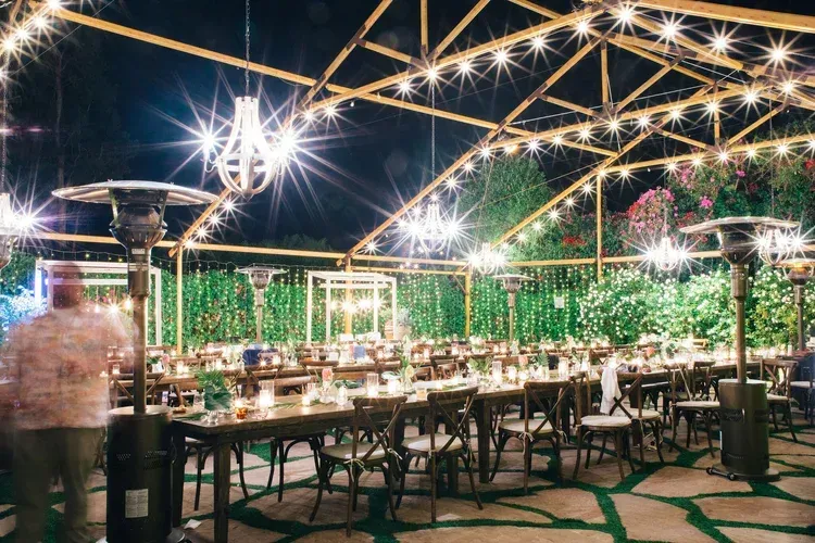 Elegant outdoor banquet setup under string lights with long tables and green foliage backdrop