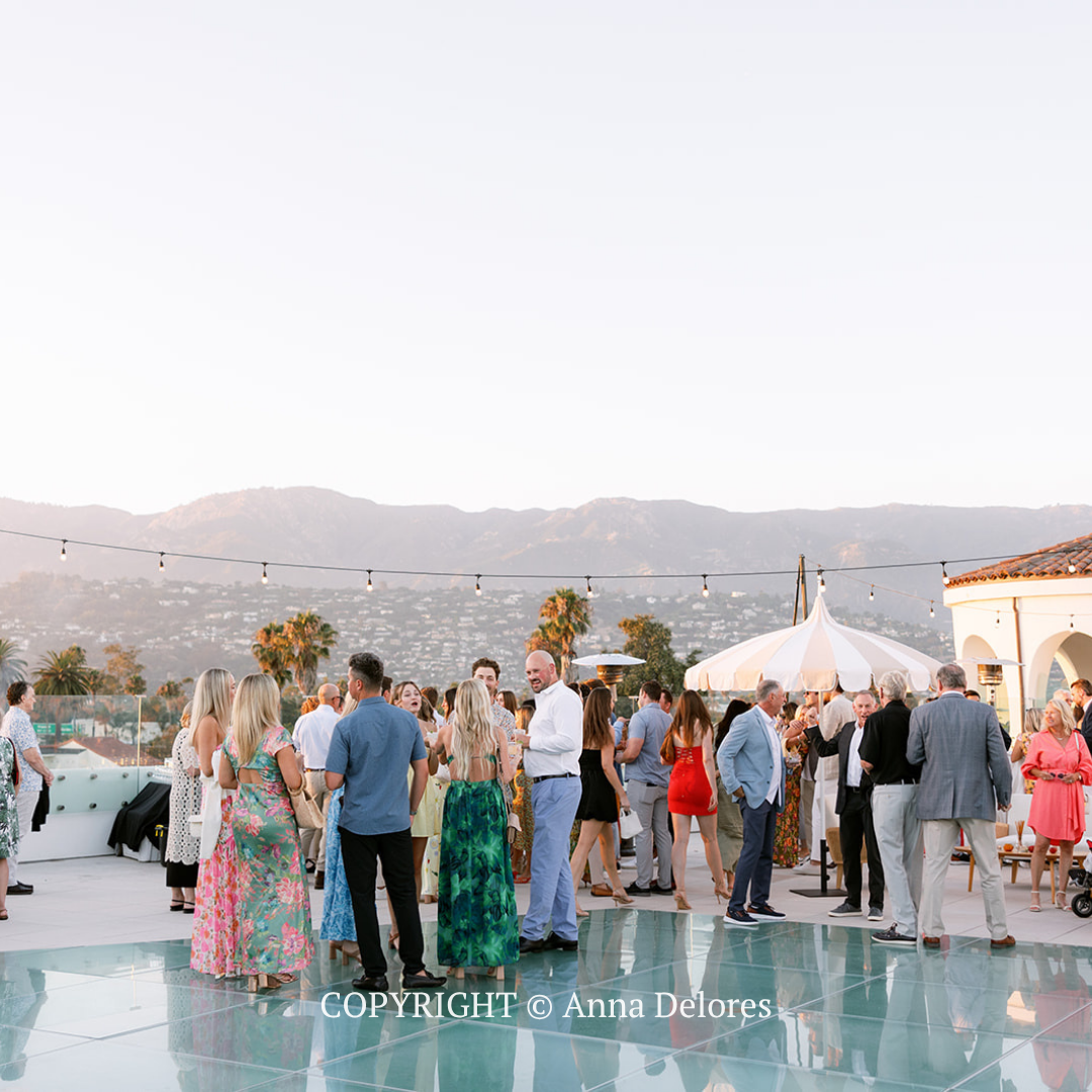 Guests mingling at an outdoor rooftop party by a pool at sunset, with mountains in the background