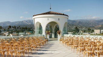 Outdoor wedding ceremony setup with gold chairs facing a white pavilion, mountains in the background