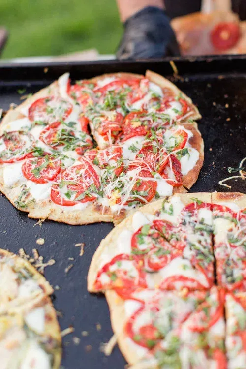 Fresh pizzas topped with tomatoes, cheese, and herbs on a hot griddle