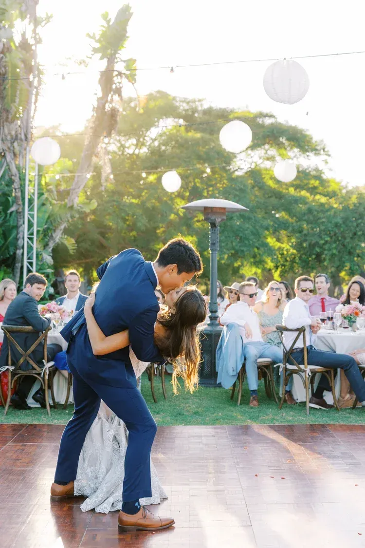 Couple dancing closely on an outdoor patio at a daytime celebration, with seated guests in the background