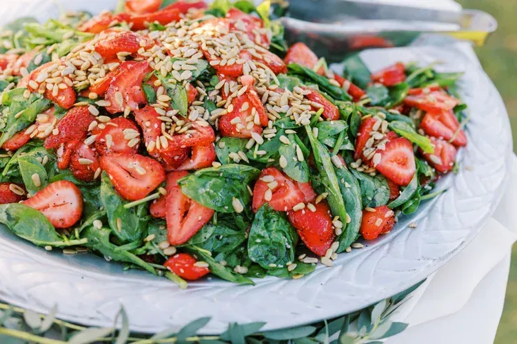 Fresh spinach salad with sliced strawberries, sunflower seeds, and dressing in a large bowl