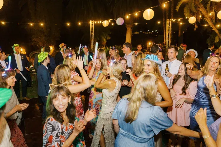 Crowd dancing at an outdoor nighttime party with string lights and glowing lanterns