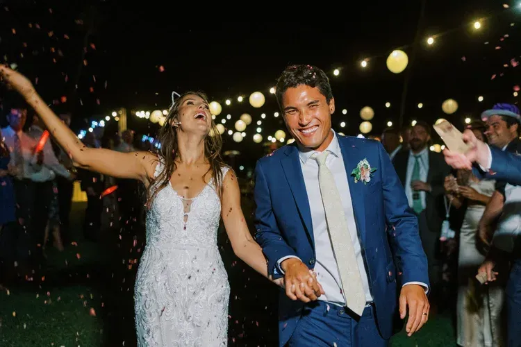 Couple in formalwear dancing joyfully at a nighttime celebration with string lights overhead