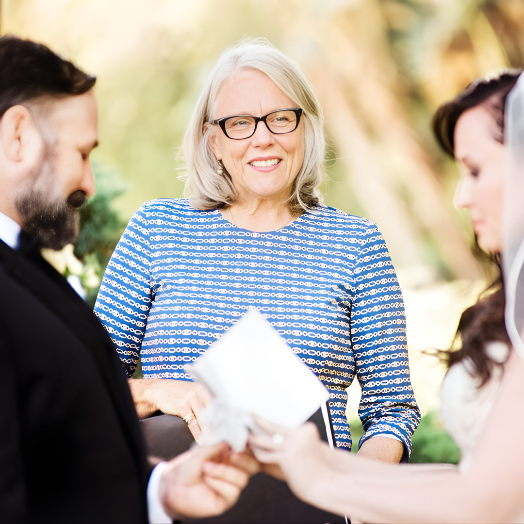 Three people exchanging papers outdoors, with a smiling woman in a blue patterned top in the center