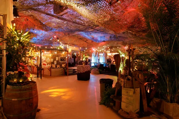 Warmly lit tropical restaurant interior with colorful ceiling fabric, plants, and glowing tables