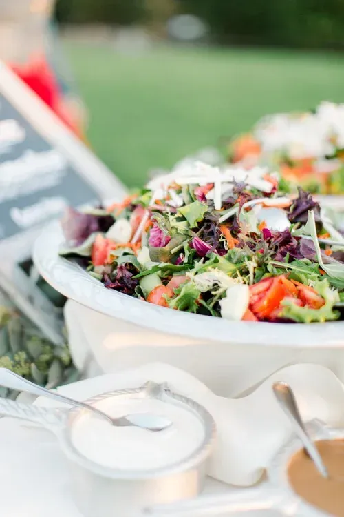Salad buffet with mixed greens, flowers, and serving spoons at an outdoor event