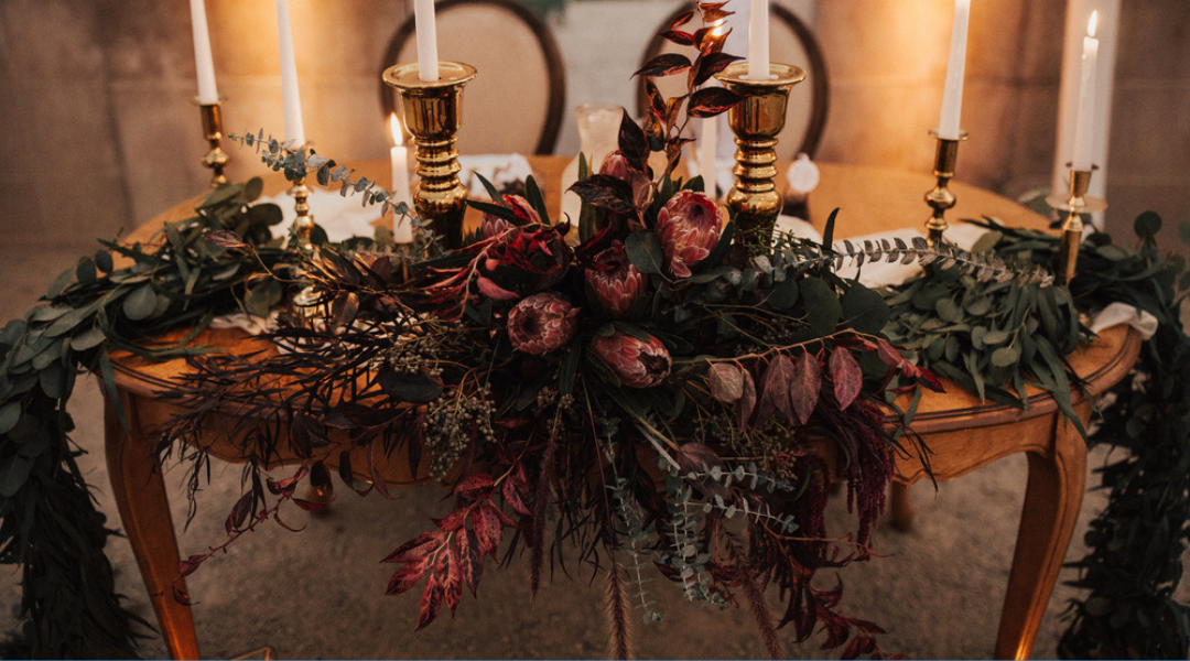 Autumn floral centerpiece with candles on a wooden table, featuring dried leaves, flowers, and greenery