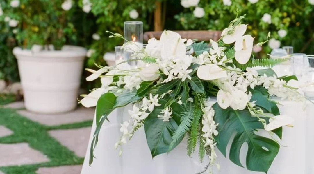 White floral centerpiece with greenery on a decorated table in a garden setting
