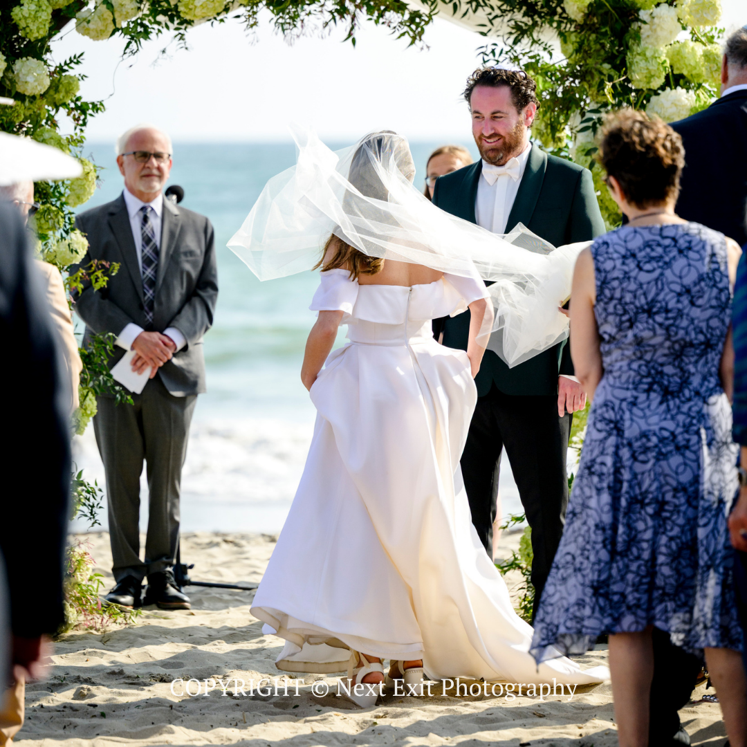 Bride and groom exchanging vows at an outdoor beach wedding under an arch