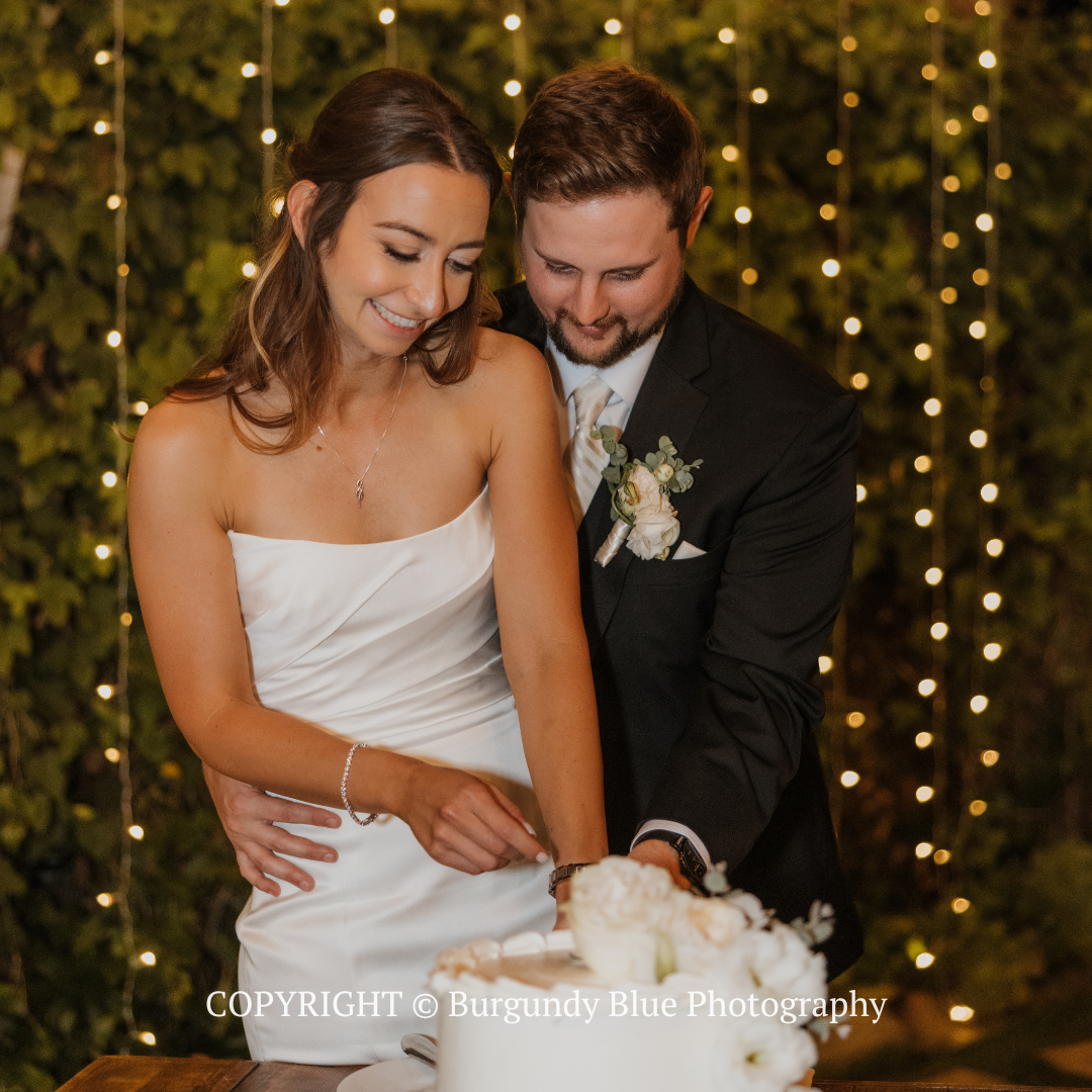 Smiling bride and groom cutting their wedding cake under warm string lights