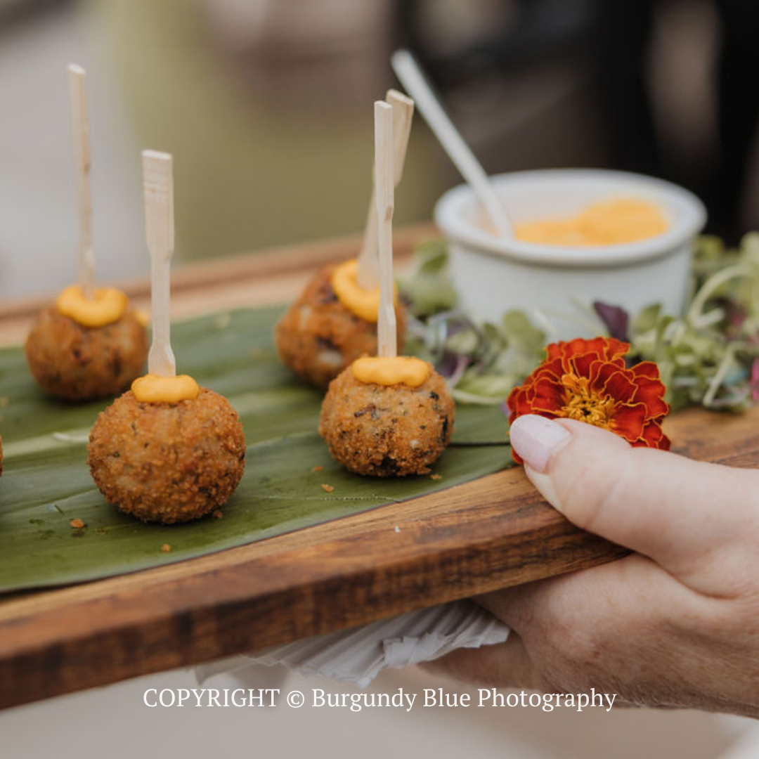 Hand placing a marigold garnish beside bite-sized appetizers on a banana leaf tray
