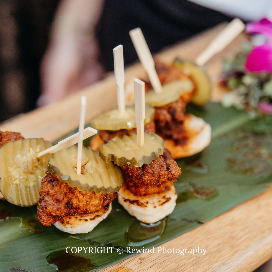 Skewered appetizer bites with pickles on a green serving board, plated for a catered event