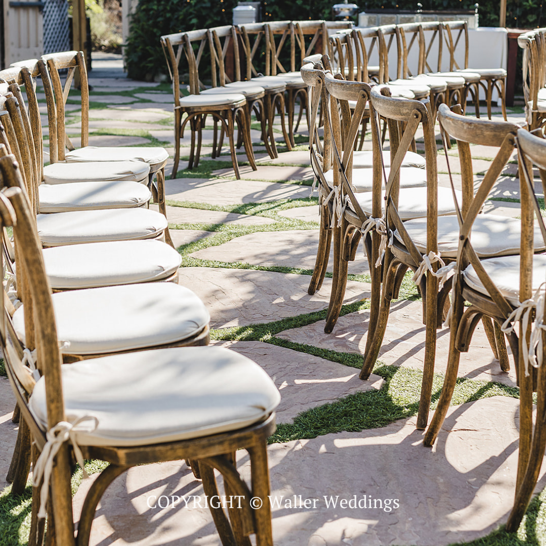 White cushioned chairs arranged along a stone aisle outdoors for a wedding ceremony