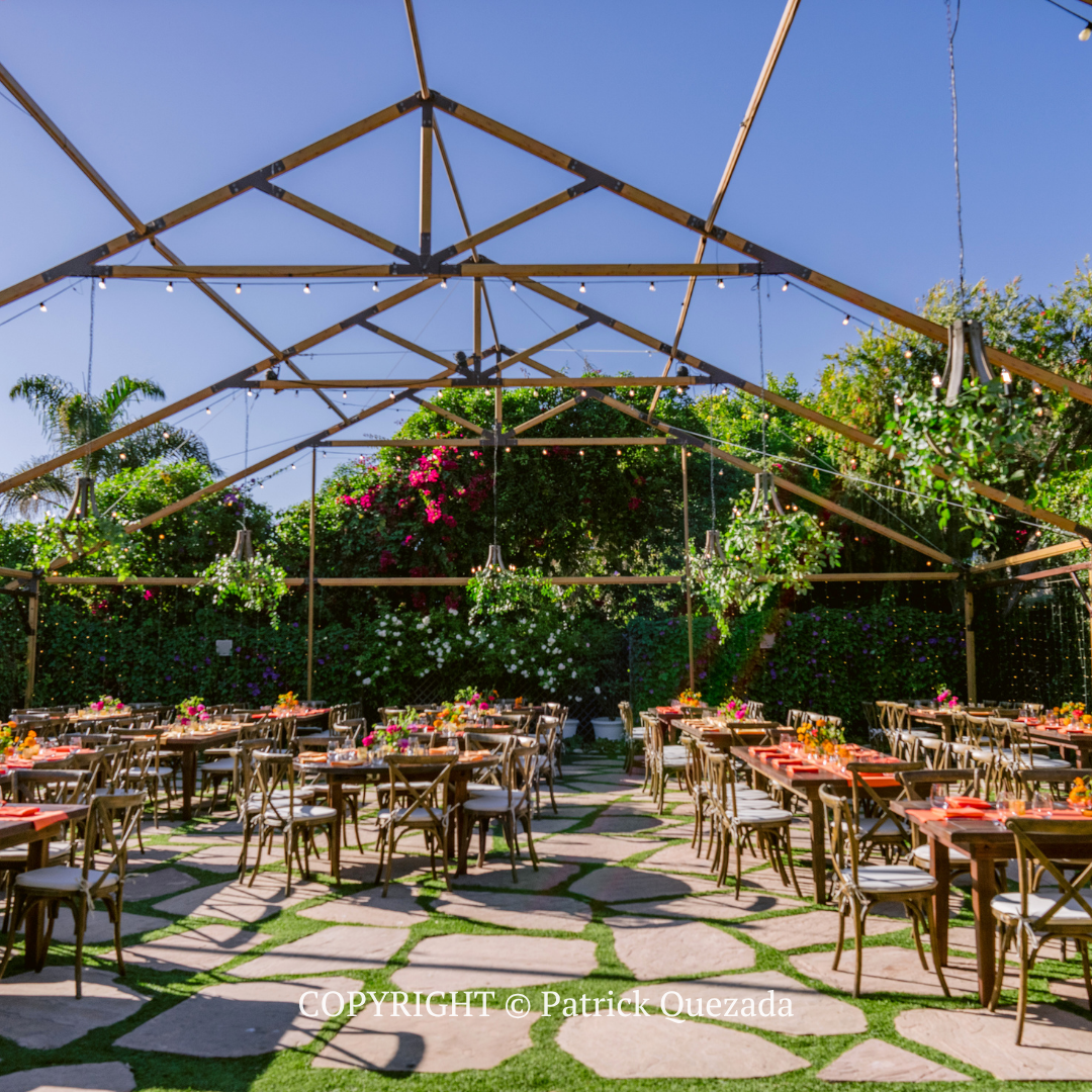 Outdoor restaurant patio with wooden tables and chairs beneath a geometric pergola and lush green vines