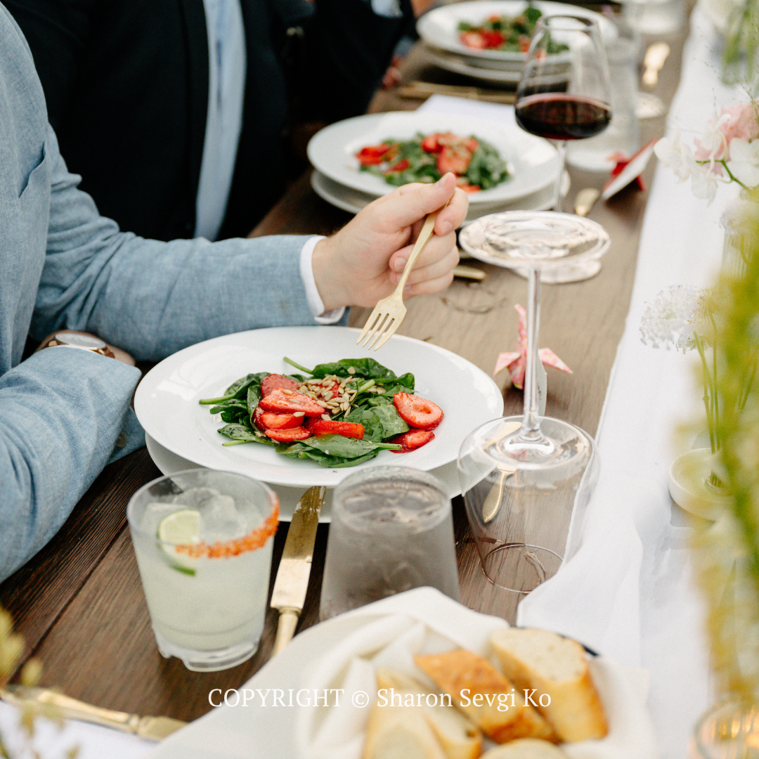 Dining table with plated salad, drinks, and a hand using a fork at a casual meal