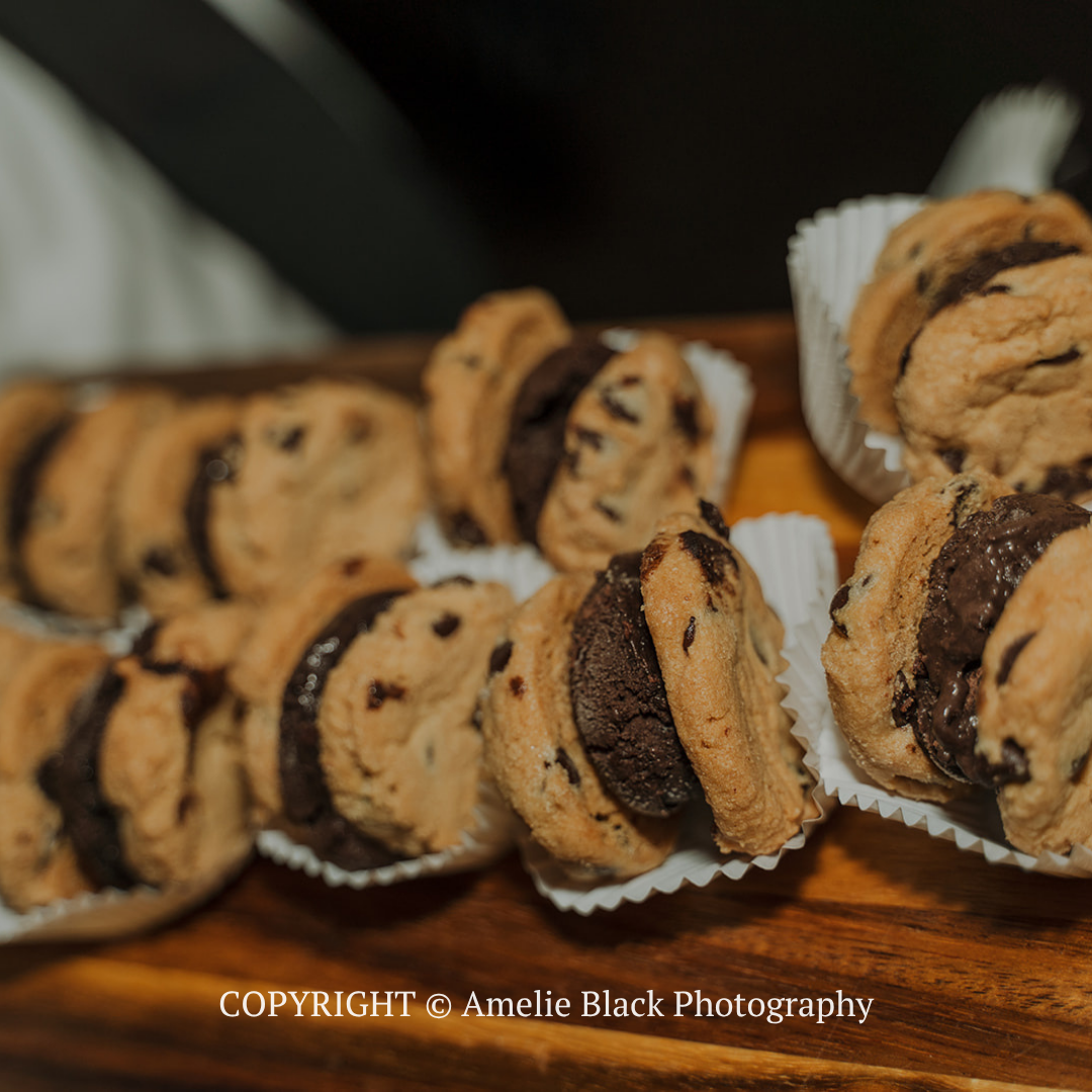 Assorted chocolate chip cookies in white paper cups on a wooden tray.